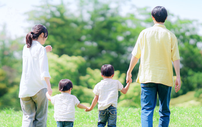公園の芝生で手をつなぎ歩く4人家族